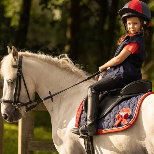 Child riding a fully tacked horse with saddle, bridle, and saddle pad in an outdoor setting
